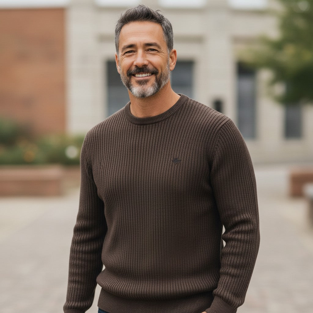 A smiling man wearing a brown ribbed O-neck sweater from WILDVINE Clothing Co. outdoors in a casual setting.