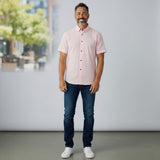 WILDVINE Clothing Co. model wearing a pink short sleeve casual button-down shirt with dark buttons and blue jeans.